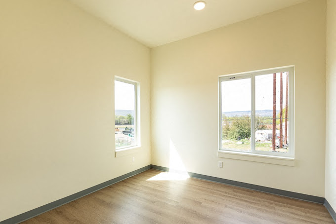 an empty living room with wood floors and two windows